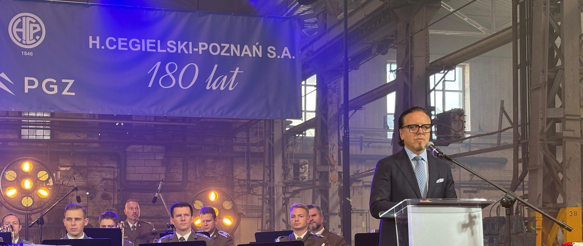 Minister Wojciech Balczun w trakcie przemówienia na jubileuszu 180-lecia H. Cegielski-Poznań S.A. Na scenie za ministrem Orkiestra Reprezentacyjna Wojsk Lądowych we Wrocławiu pod dyrekcją ppłk. Krzysztofa Żeleśkiewicza.