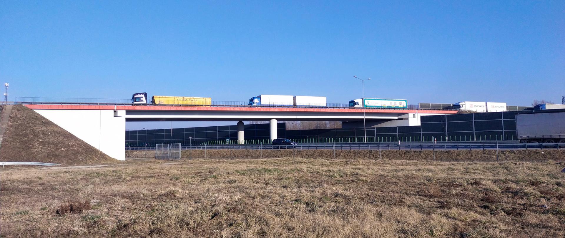 widok na wiadukt w ciągu drogi krajowej numer 50 - węzeł Wiskitki. Wiaduktem przemieszczają się samochody ciężarowe. Pod wiaduktem widoczna jest autostrada A2 