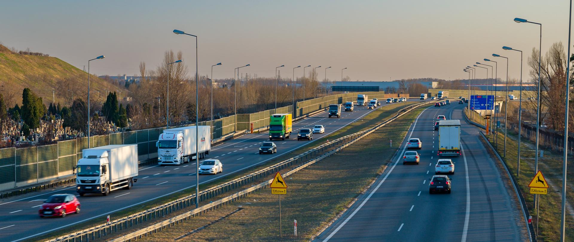 Dwujezdniowa autostrada rozdzielona pasem zieleni z barierkami. Duży ruch samochodów osobowych i ciężarowych w obu kierunkach. 