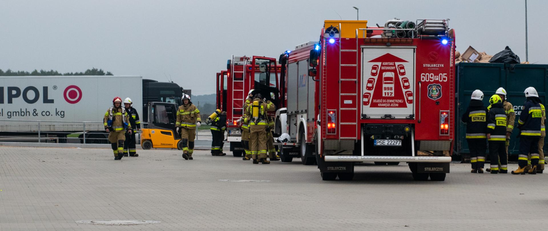 Na placu firmy samochody strażackie i ratownicy oraz Tir obok pojazdu ratowniczo - gaśniczego kontener