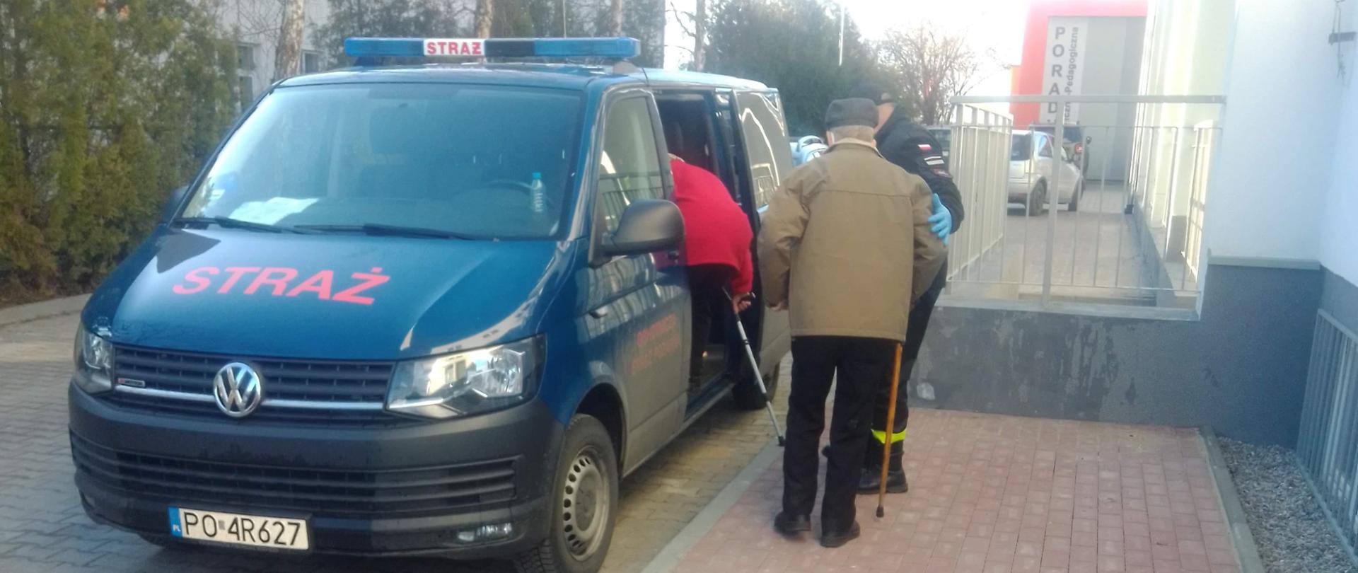 Na zdjęciu widać pojazd pożarniczy Ochotniczej Straży Pożarnej w Kawęczynie, którym są transportowane osoby na szczepienie. Obok pojazdu widać starszą osobę, która będzie transportowana. Tuż obok widać strażaka OSP Kawęczyn, który pomaga wsiąść drugiej osobie do pojazdu.
