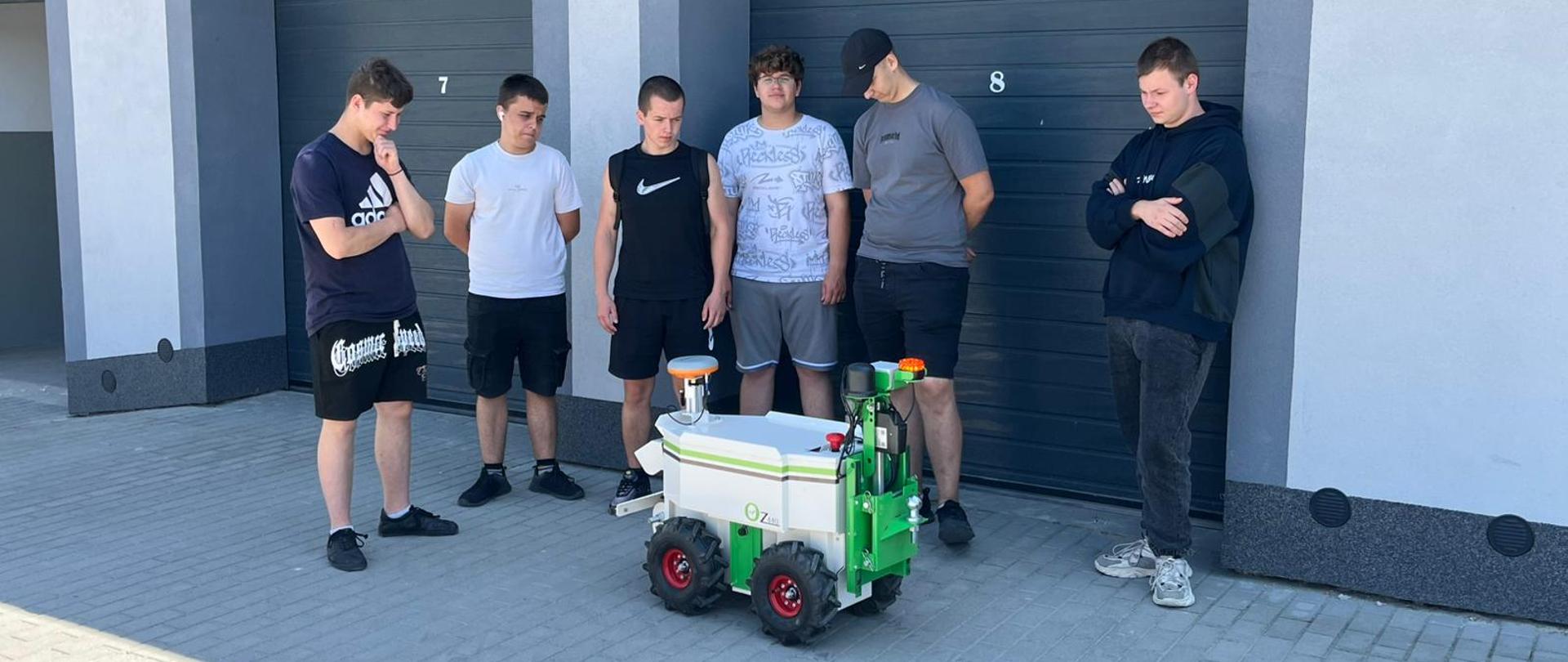 Grupa uczniów obserwuje autonomiczny robot rolniczy podczas prezentacji na placu szkoleniowym.