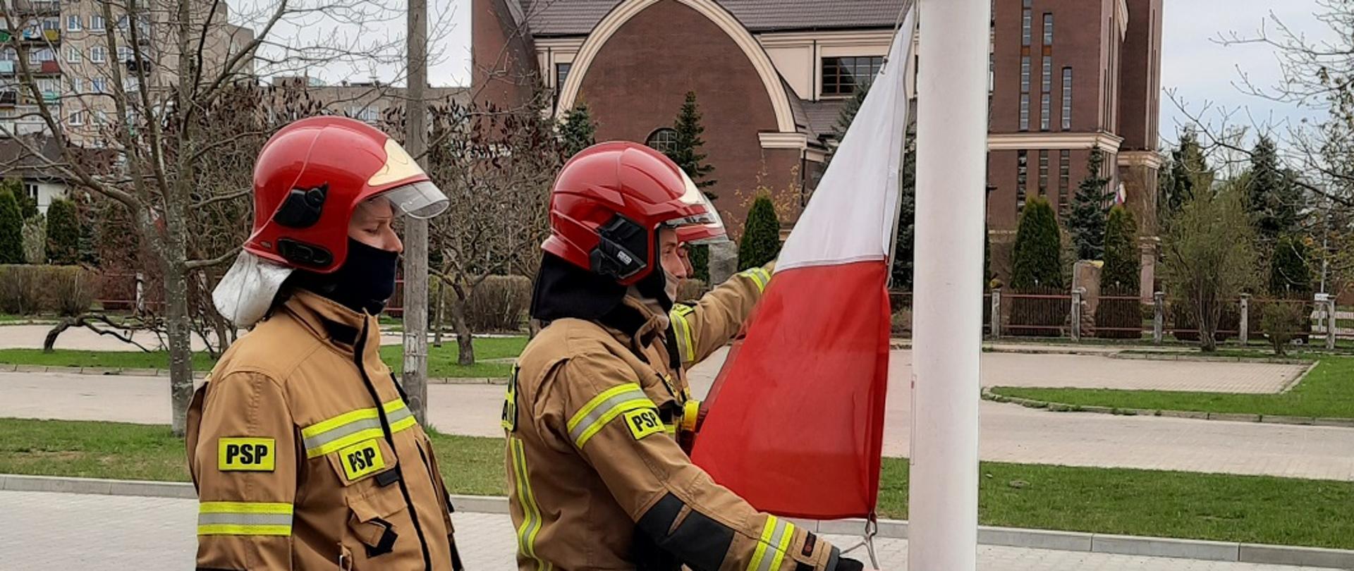 Zdjęcie przedstawia 3 strażaków zawieszających flagę na maszt