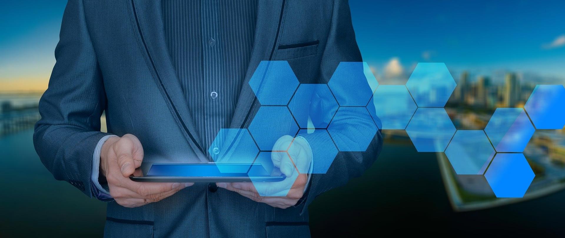 Mężczyzna w garniturze trzymający w dłoniach tablet.