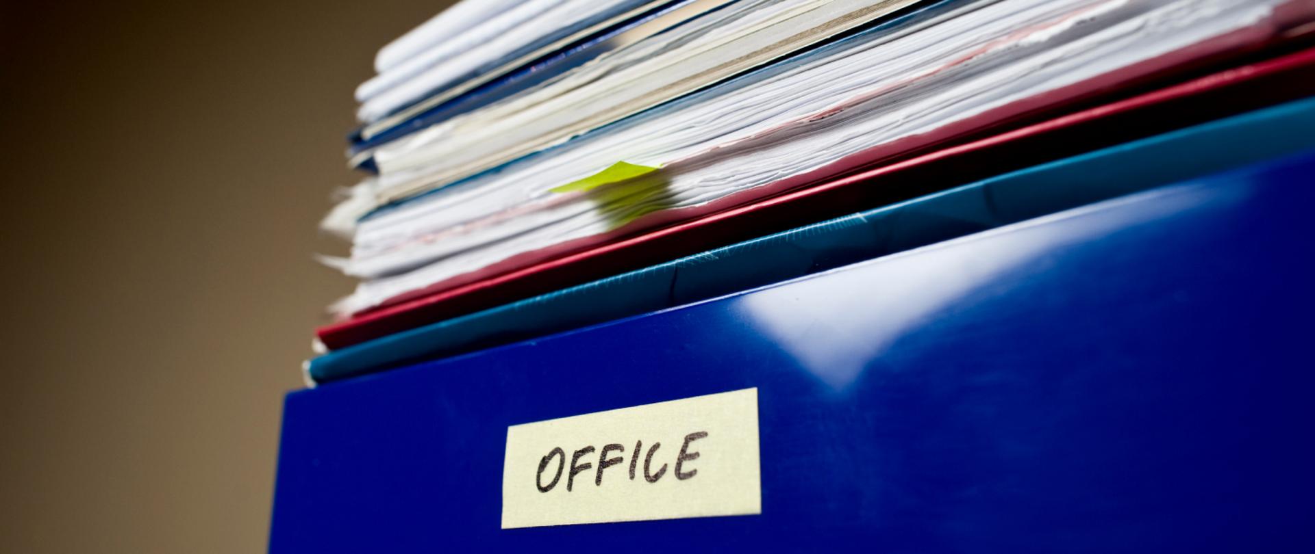 Na grafice wiać stos dokumentów. Na jednym z nich napis OFFICE.