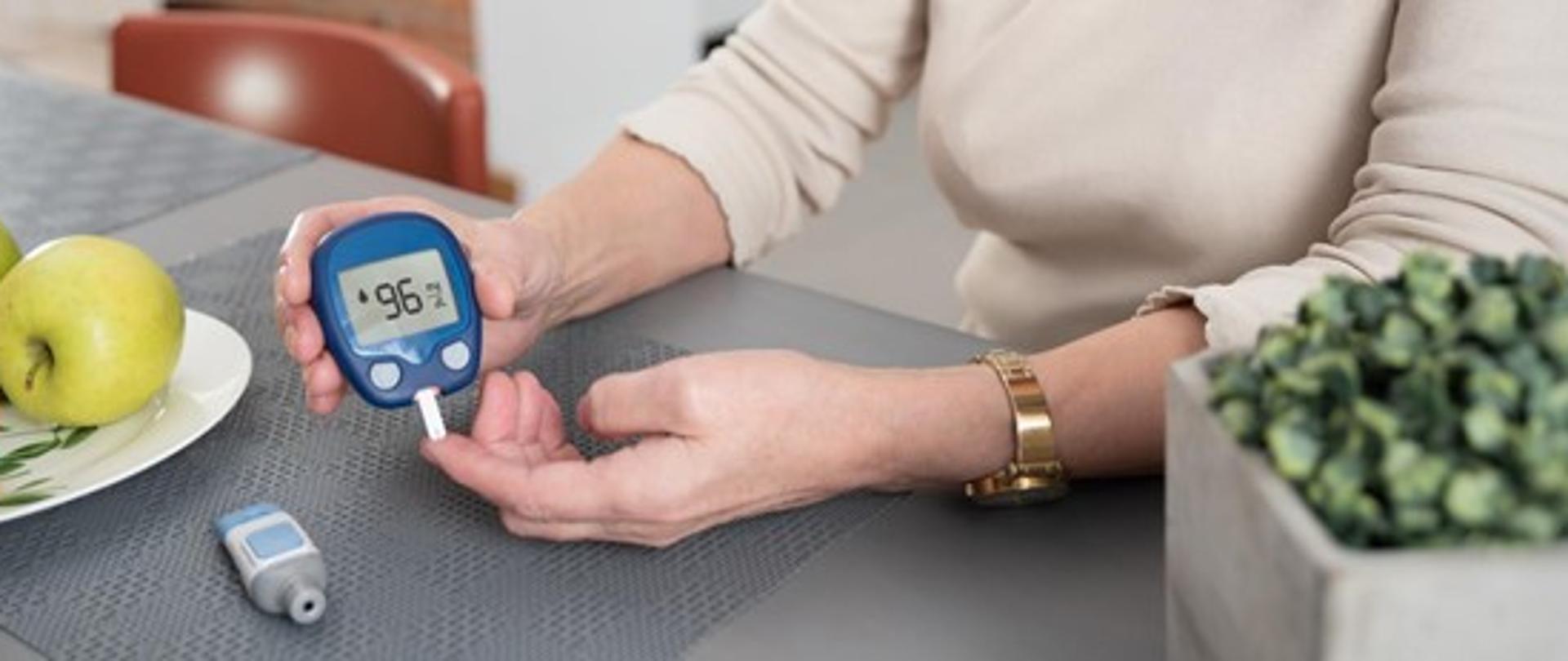 Zdjęcie przedstawia kobiece dłonie trzymające glukometr.