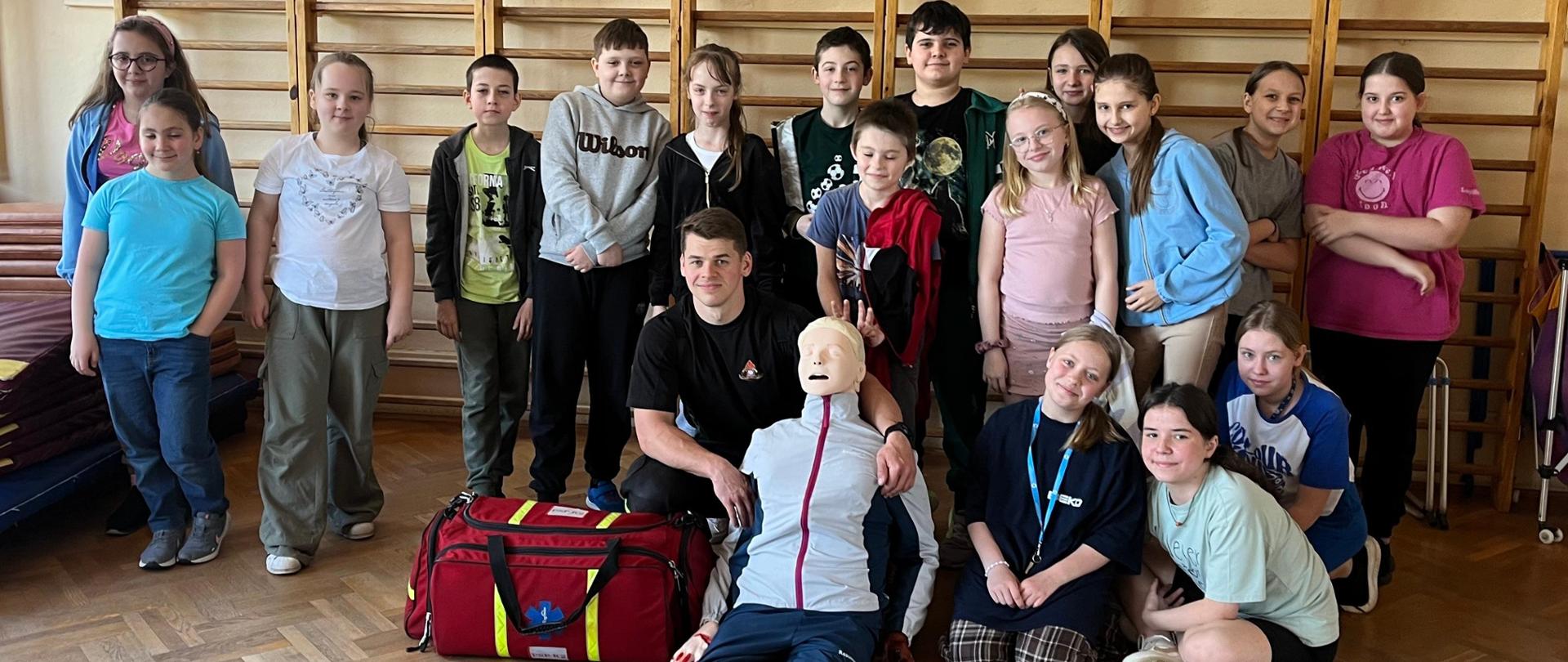 Odwiedziny w Szkole Podstawowej Nr 1 w Sokołowie Podlaskim 09.04.2024 r. - wspólne zdjęcie strażaka z uczniami w sali gimnastycznej