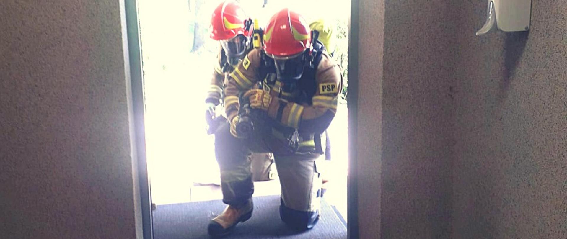 Zdjęcie przedstawia dwóch strażaków ratowników w aparatach tlenowych podczas wejścia do pomieszczenia 