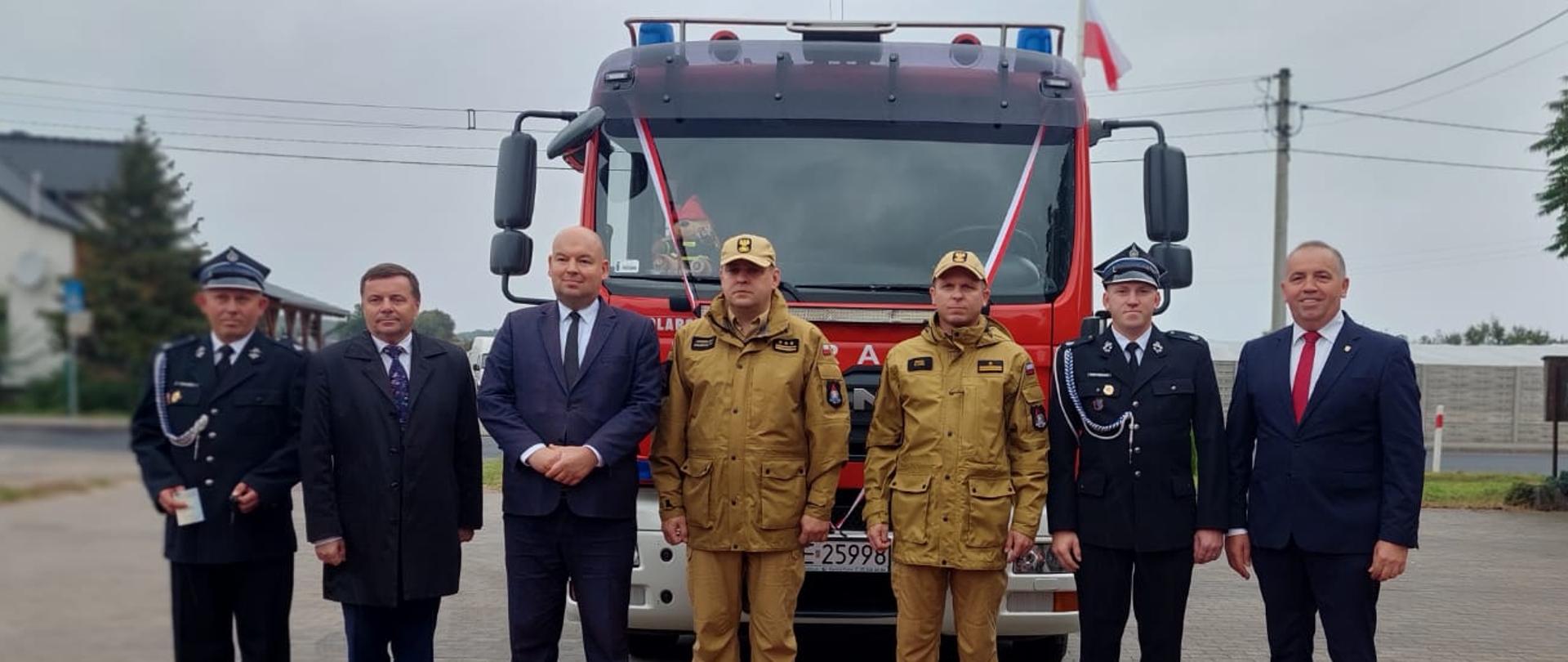 grupa mężczyzn strażaków i cywili sto przed samochodem strażackim