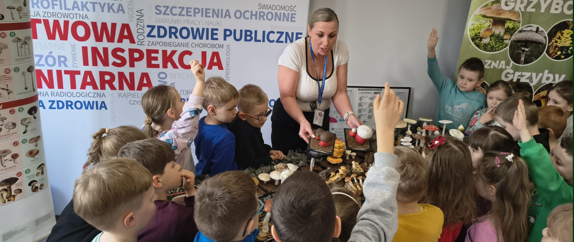 Dni otwarte Powiatowej Stacji Sanitarno-Epidemiologicznej w Rzesowie. Wystawa grzybów, wokół dzieci przedszkolne. Pracownik opowiadający dzieciom o grzybach.