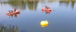 Zdjęcie przedstawia 2 balony wypornościowe znajdujące się na powierzchni wody, przymocowane przez nurków do zanurzonego pojazdu. W tle dwie łodzie motorowe ze strażakami.