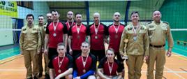 Strażacy, zawodnicy drużyny, która zajęła 3 miejsce pozują do zdjęcia razem z komendantami na boisku hali sportowej.