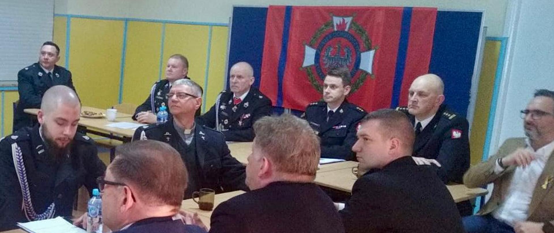 Na zdjęciu znajdują się siedzący przy stoach druhowie OSP Wąbrzeźno, podczas zabrania sprawozdawczego. W zebraniu udział biorą Zastępca Kujawsko-Pomorskiego Komendanta Wojewódzkiego PSP st.bryg. Sławomir Herbowski, p.o. Komendant Powiatowy PSP w Wąbrzeźnie kpt. Robert Stasiak oraz Burmistrz Wąbrzeźna Tomasz Zygnarowski.