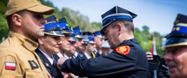 Na zdjęciu widoczni prezes zarządu oddziału wojewódzkiego Związku Ochotniczych Straży Pożarnych Rzeczypospolitej Polskiej województwa małopolskiego i zastępca małopolskiego komendanta wojewódzkiego Państwowej Straży Pożarnej wręczający strażakom odznaczenia resortowe. Komendant w galowym granatowym mundurze i w czapce rogatywce. Strażacy odbierający odznaczenia ubrani w galowe granatowe mundury i w czapkach rogatywkach oraz ubrania służbowe koloru piaskowego.