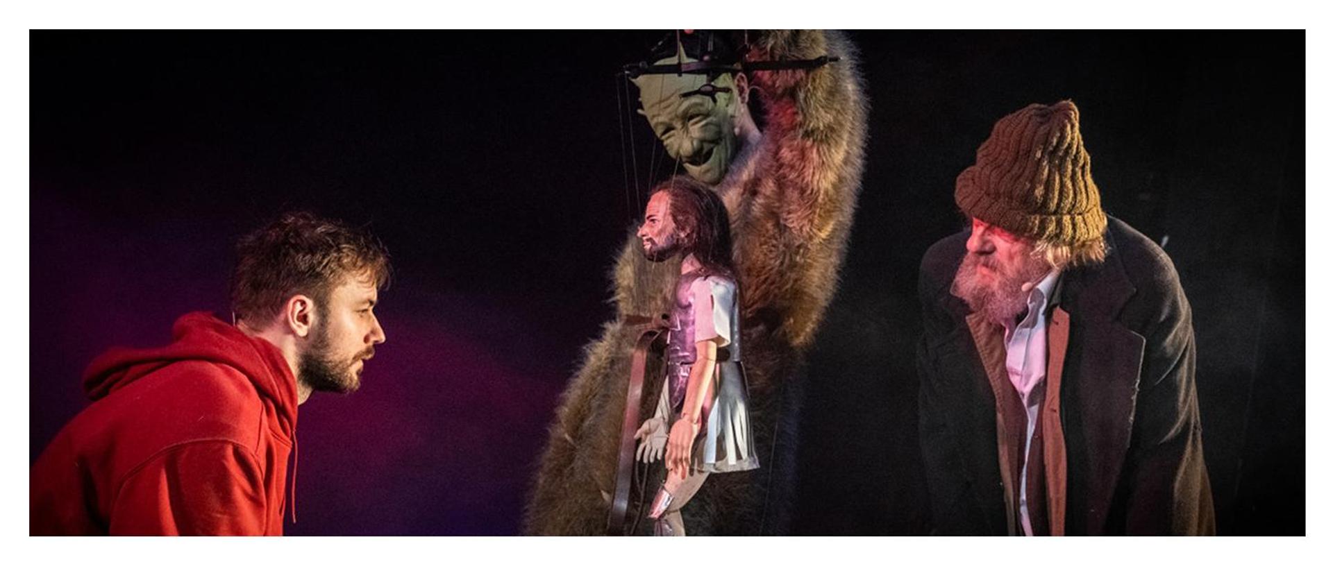 3 aktorów podczas spektaklu, środkowy aktor ma na sobie maskę diabła i trzyma w ręku lalkę w zbroi