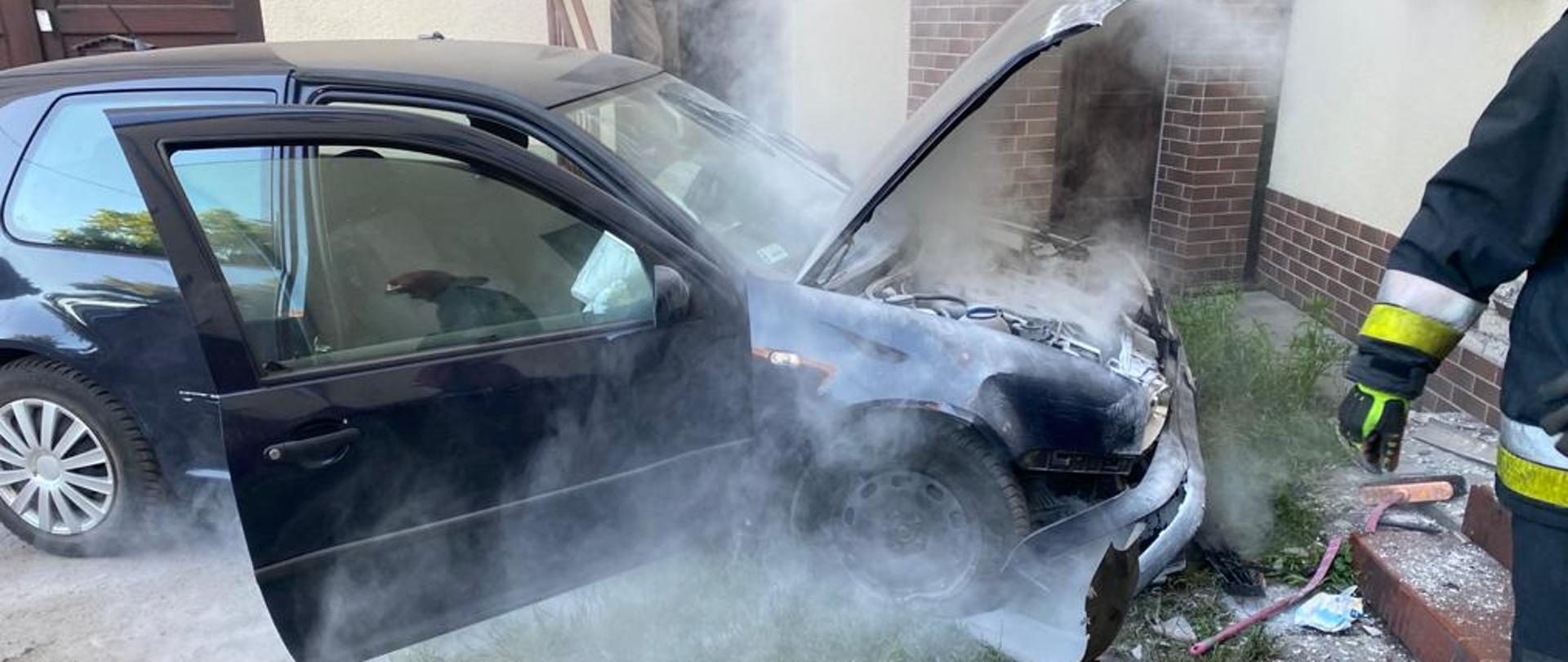 granatowe auto z otwartymi prawymi drzwiami oraz maską komory silnika, osnute chmurą proszku gaśniczego