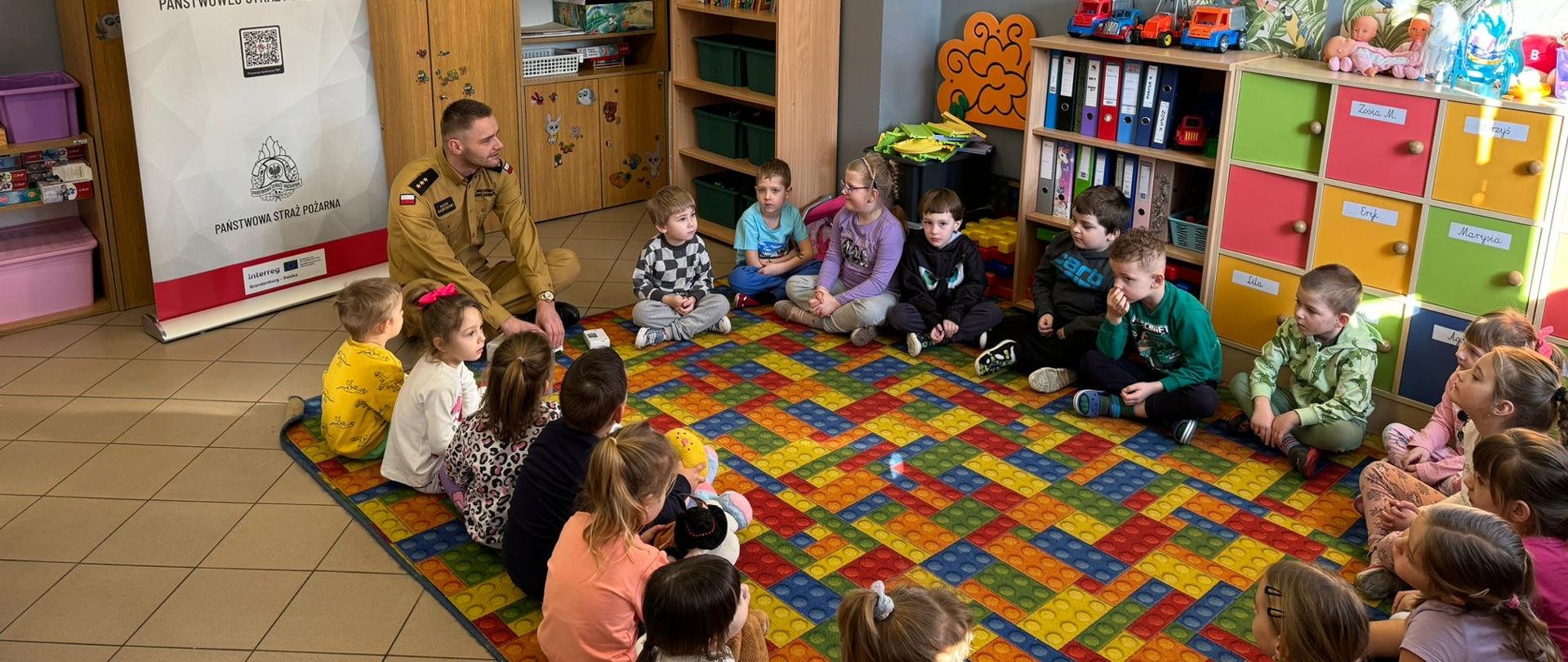 Zdjęcie przedstawia strażaka przedstawiającego zagadnienia związane z zajęciami dzieciom w klasie.