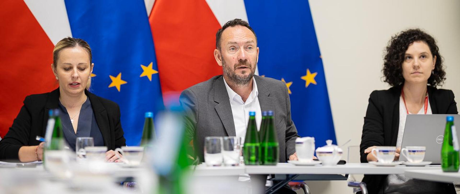 Przy stole prezydialnym na tle flag wiceminister MSWiA Tomasz Szymański.