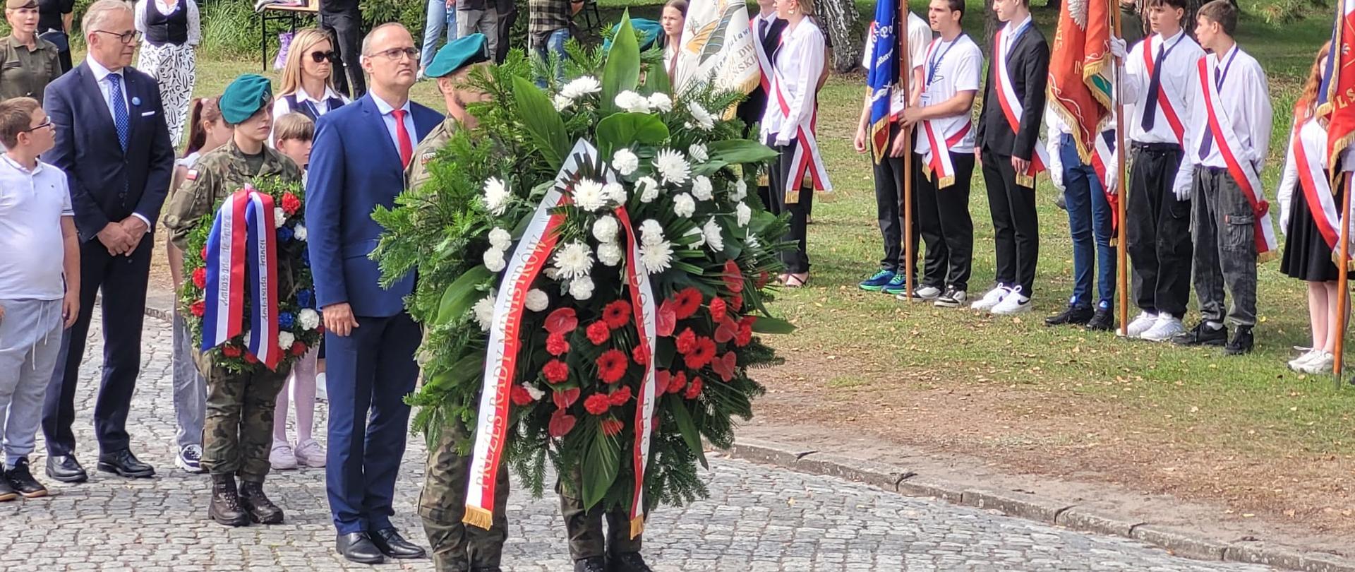 żołnierze trzymają biało czerwony wieniec, za nimi kilkoro ludzi