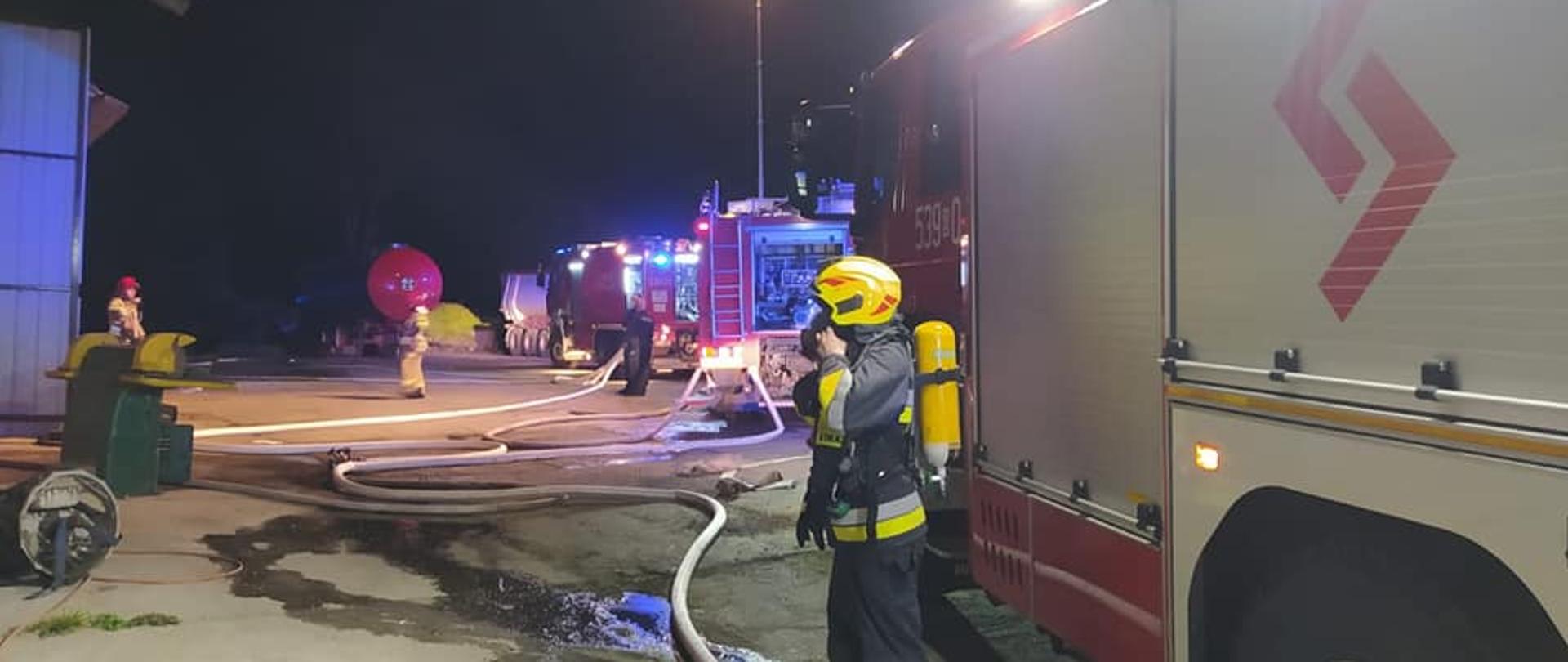 teren akcji pożaru. Widać ubierającego si.e do działań ratownika na tle ustawionych pojazdów pożarniczych