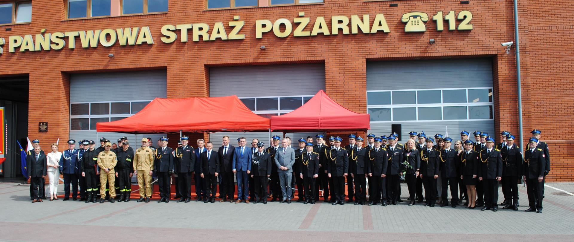 Zdjęcie grupowe strażaków oraz zaproszonych gości na tle budynku Komendy
