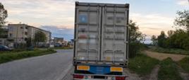 Fotografia przedstawia tył nieprawidłowo zaparkowanej ciężarówki z kontenerem, stojącej przy bocznej drodze