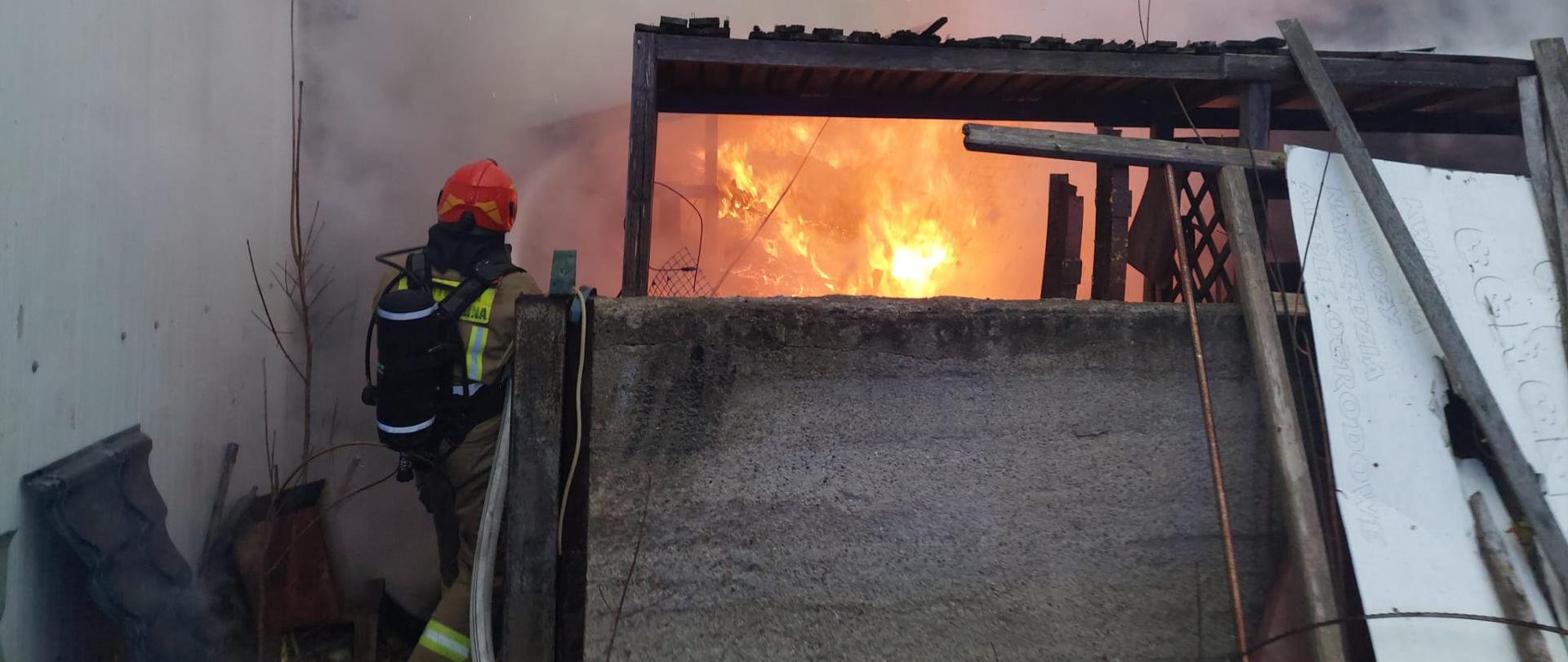nad zdjęciu widać strażaka gaszącego paląca się wiatę