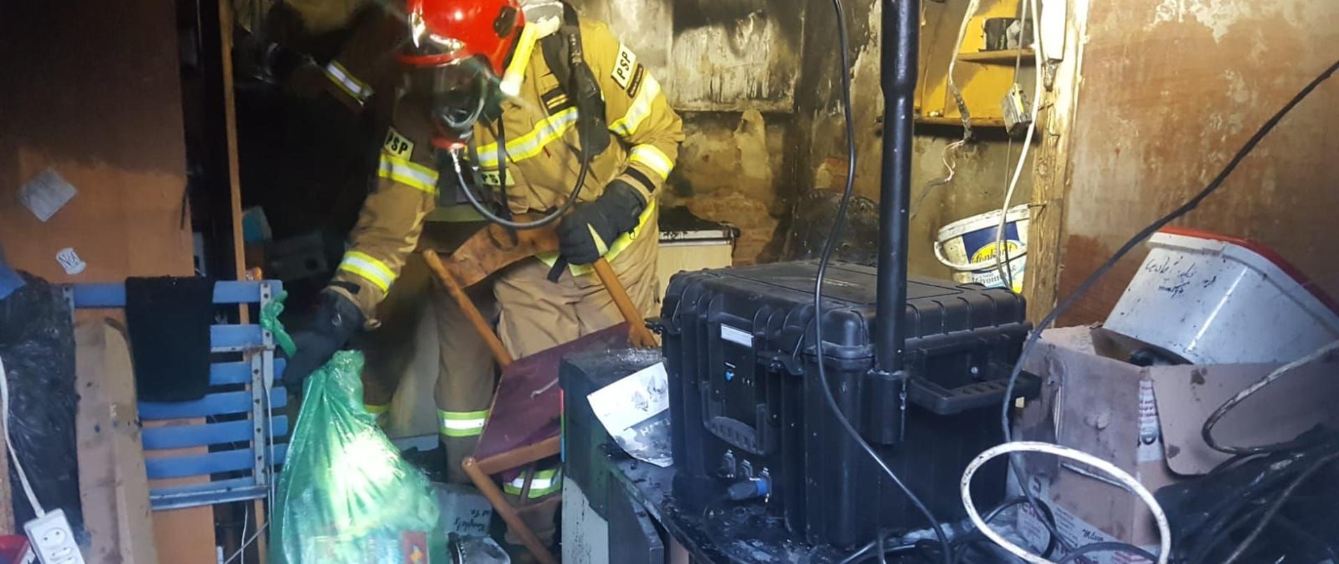 Wnętrze budynku, strażak wynosi nadpalone przedmioty.