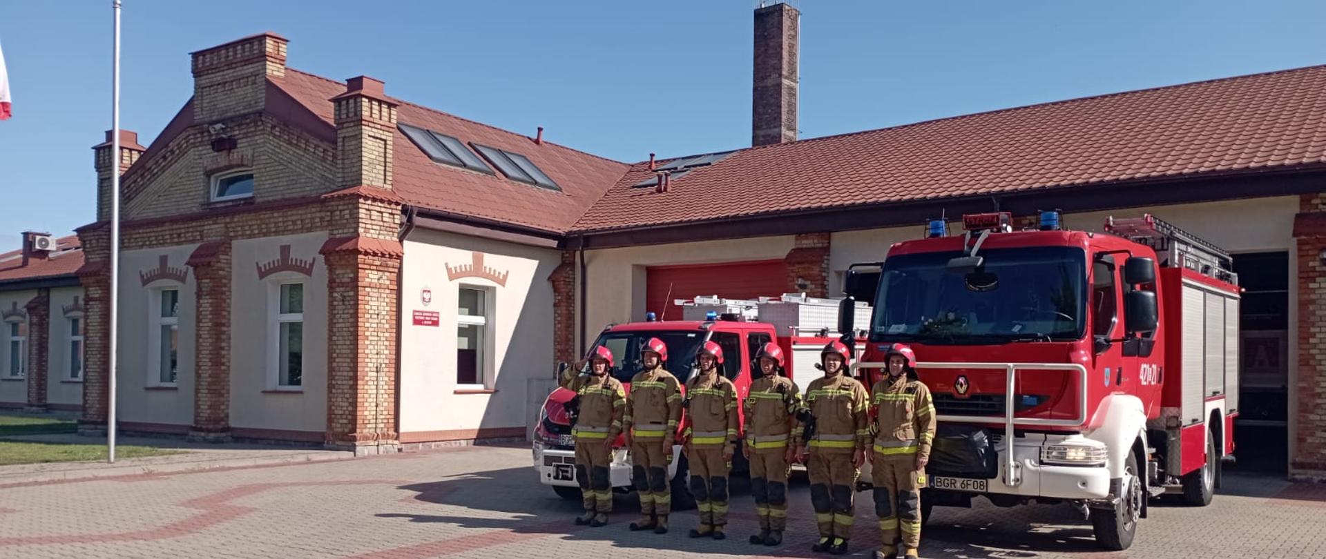 Strażacy PSP stoją na baczność pod strażnicą.