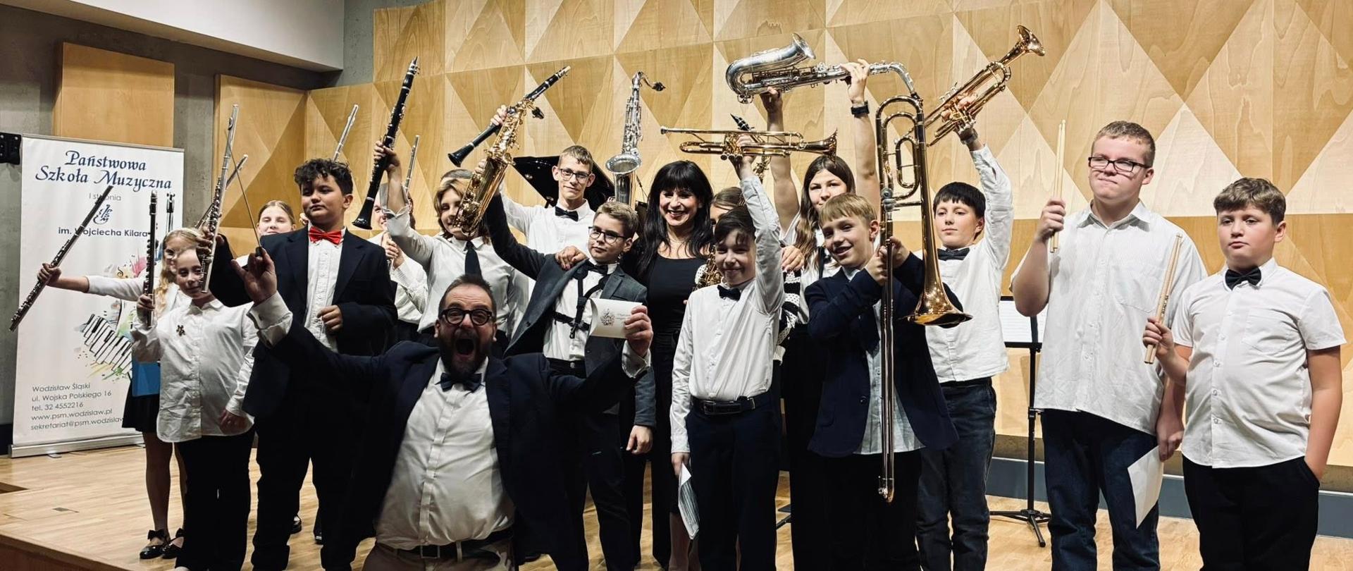 grupa dzieci na scenie szkoły muzycznej, trzymają w rękach instrumenty