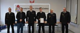 Stojący w jednej linii sześciu mężczyzn. Pięciu w mundurach. Pośrodku trzymający dyplom druh Przemysław Kaczmarczyk z jednostki OSP Kietlin.
