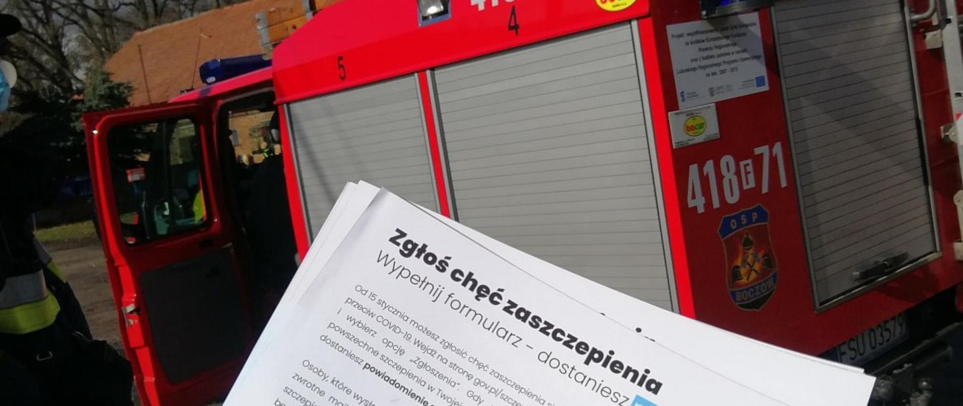Ulotka o szczepieniach na tle pojazdu strażackiego. 