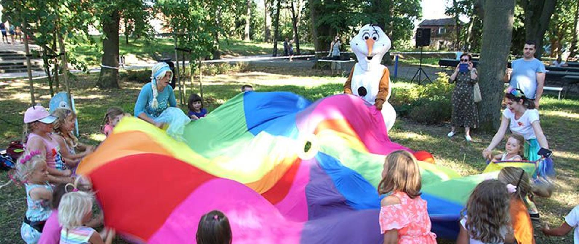 Dzieci w parku bawiące się kolorowym materiałem.