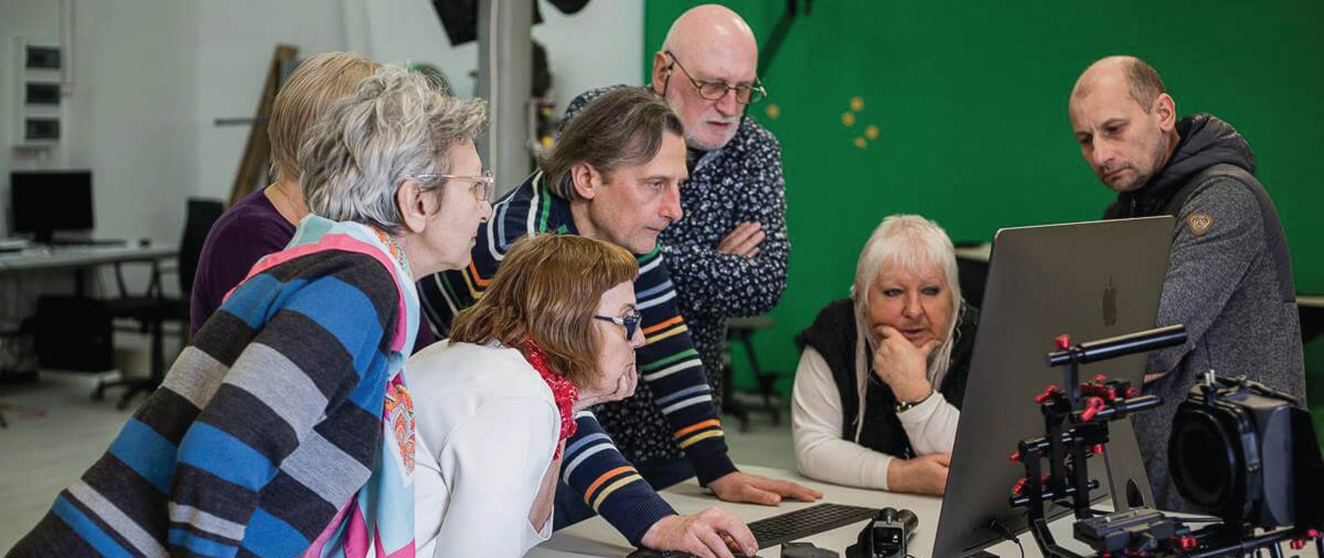 Sześcioosobowa grupa seniorów pracuje przy stole inżynierskim pod okiem prowadzącego zajęcia