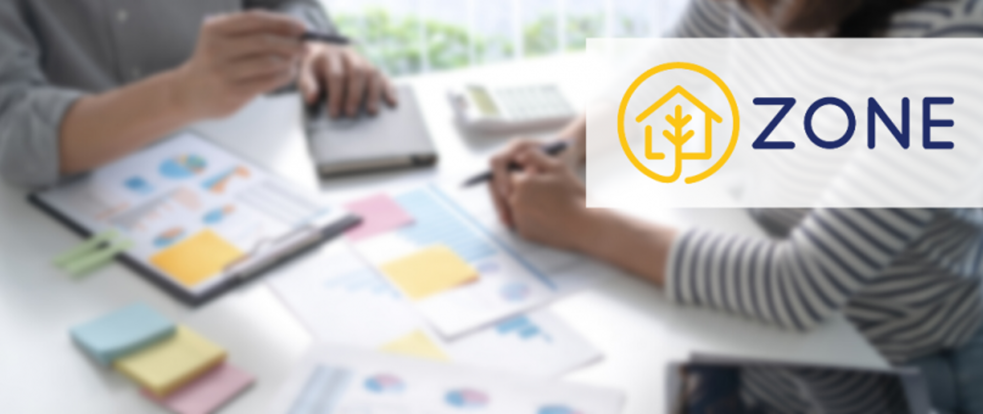 Dwie osoby siedzące przy stole, omawiające dokumenty i wykresy; jedna wskazuje na dokument długopisem, na stole widoczny kalkulator, po prawej stronie logo „ZONE” z ikoną domu i drzewa.