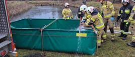 Strażacy sprawiający zbiornik brezentowy i napełniający go wodą