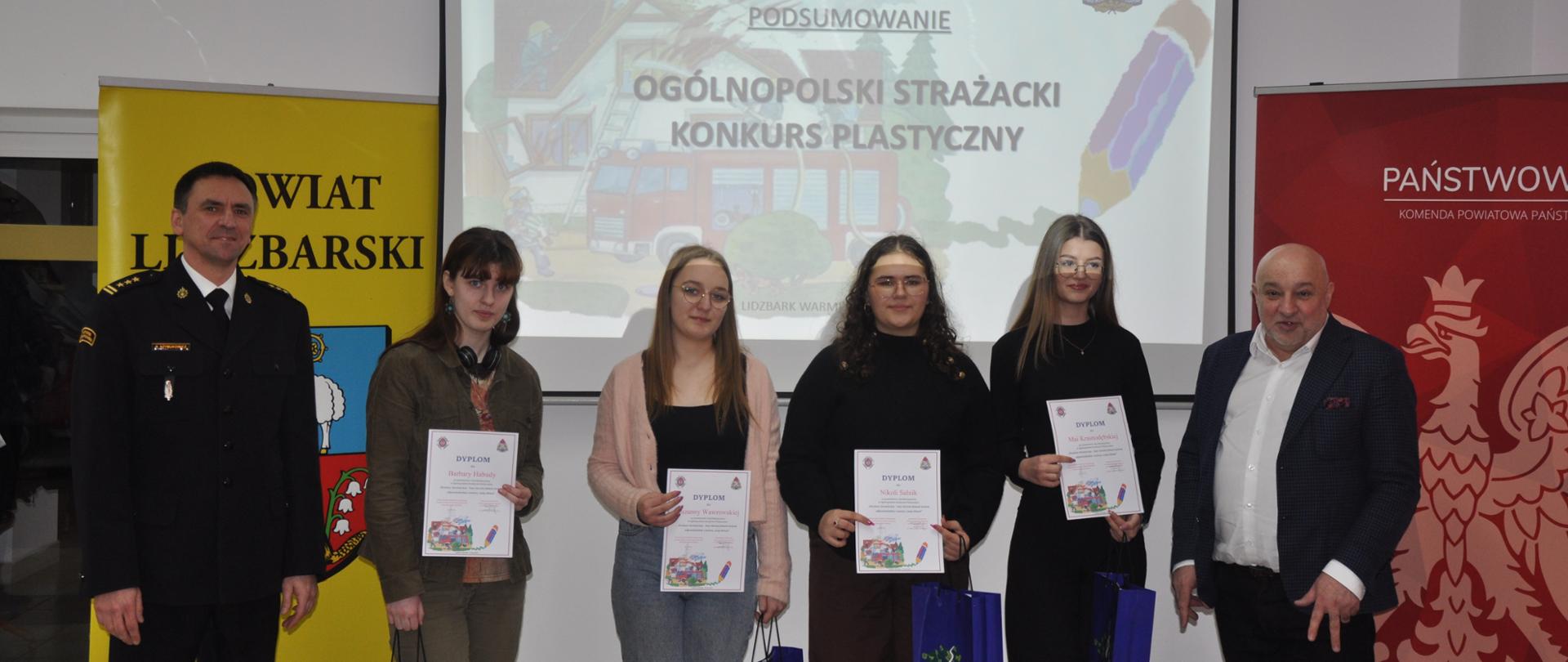 Zdjęcie przedstawia grupę wyróżnionych dziewcząt wraz z Komendantem Powiatowym PSP oraz Wicestarostą Powiatu Lidzbarskiego