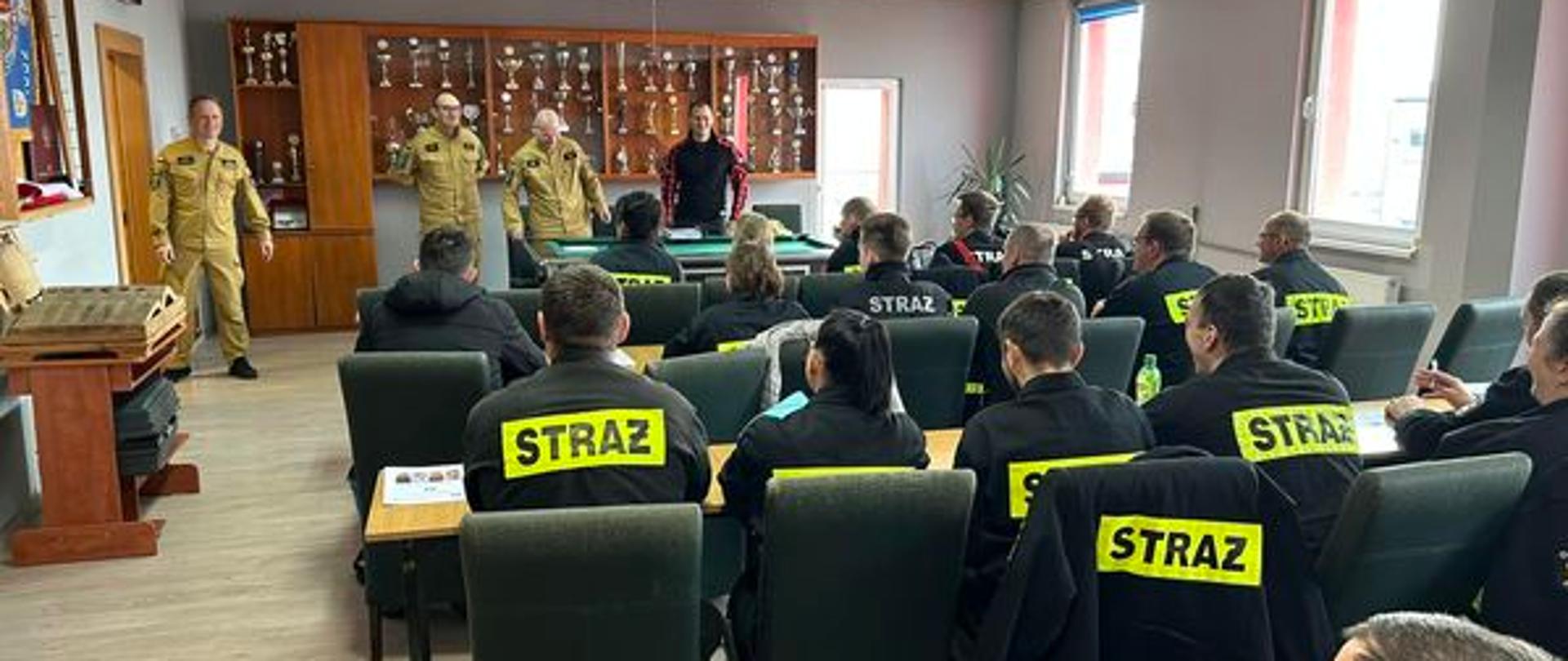 Na zdjęciu znajdują się strażacy siedzący w ławkach