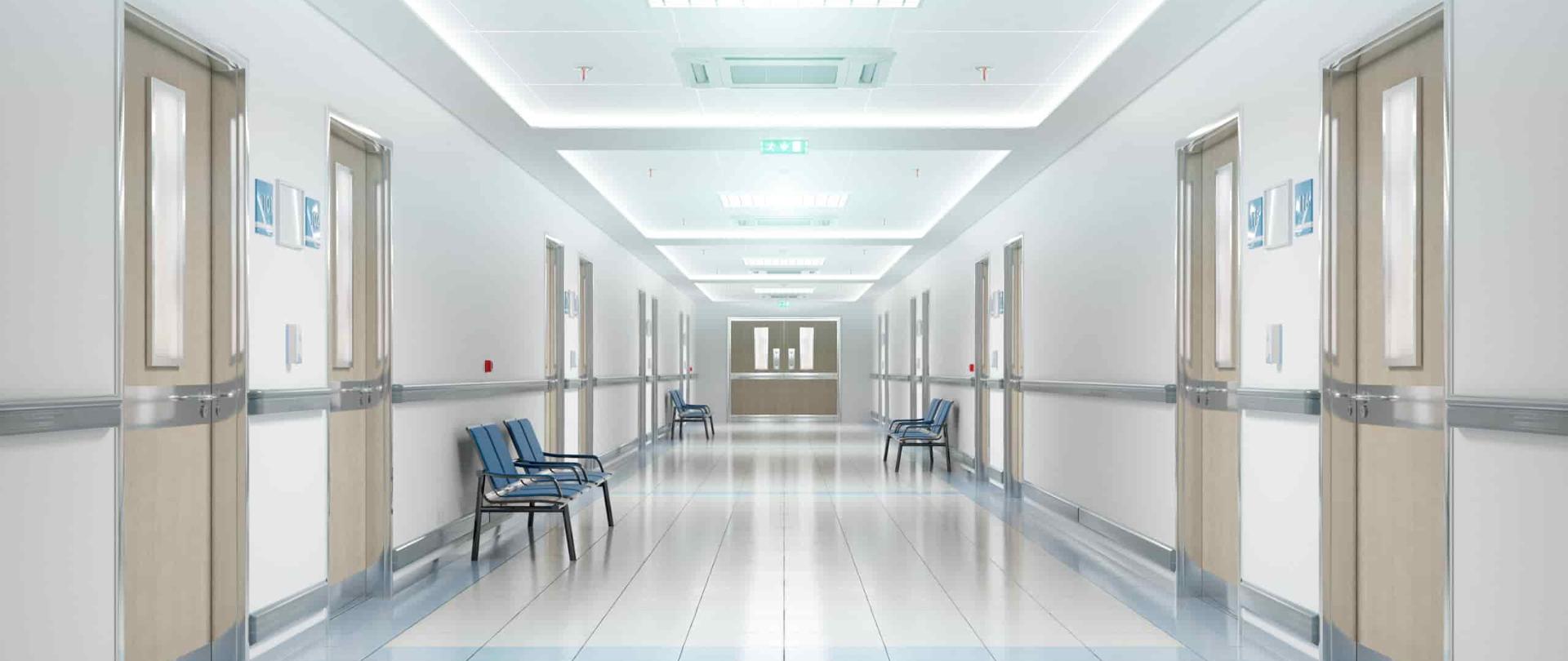Na zdjęciu przedstawiono korytarz znajdujący się w szpitalu. Po obu stronach znajdują się krzesła oraz drzwi. 