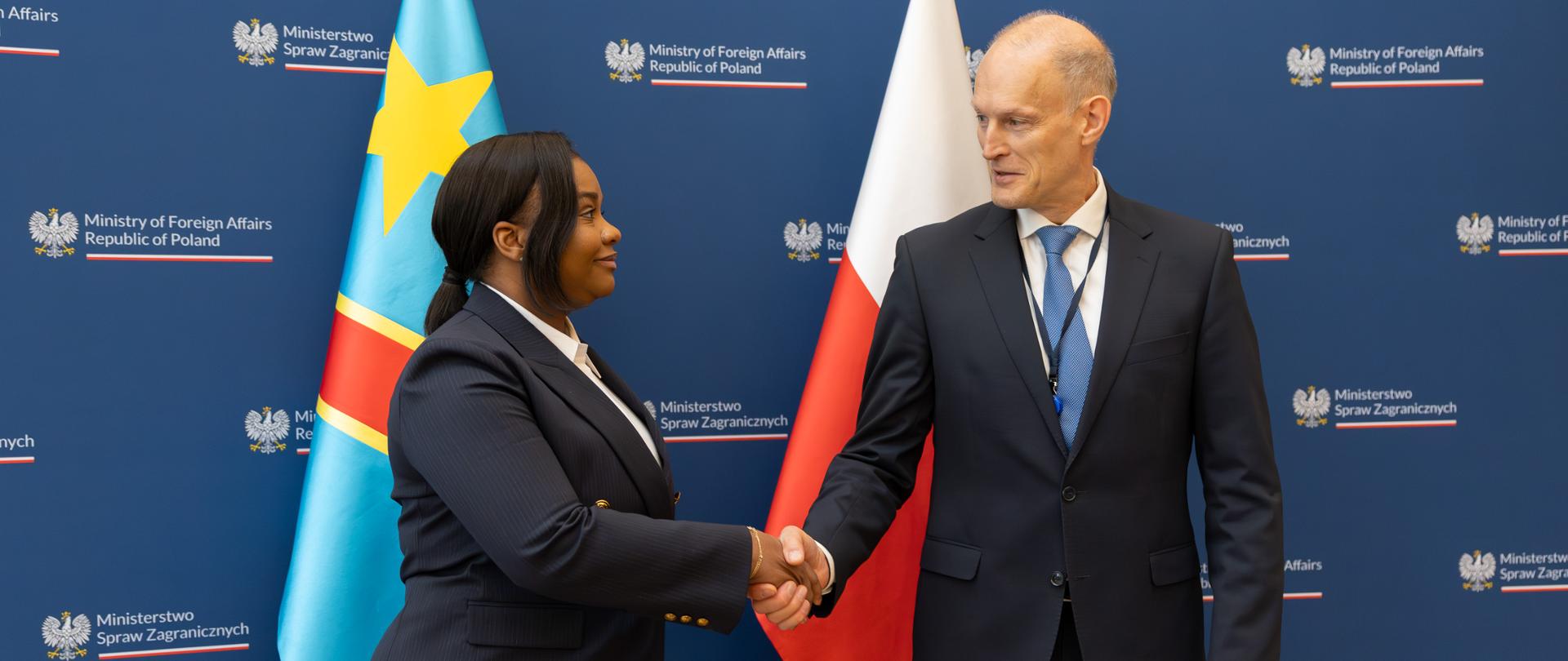 Na zdjęciu rękę podają sobie: Podsekretarz Stanu Wojciech Zajączkowski oraz Wiceministra Spraw Zagranicznych, Współpracy Zagranicznej, Frankofonii i Diaspory Kongijskiej Demokratycznej Republiki Konga Noëlli Ayeganagato Nakwipone. W tle ścianka z logotypem MSZ oraz dwie flagi. 