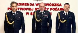 od prawej w mundurach galowych Komendant Powiatowy PSP w Stargardzie, Zachodniopomorski Komendant Wojewódzki, pełniący obowiązki zastępcy Komendanta Powiatowego PSP w Stargardzie na tle ściany z logo PSP i napisem Komenda Wojewódzka Państwowej Straży Pożarnej w Szczecinie