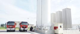 Na pierwszym tle zbiorniki z gazem LNG obok stoją dwa samochody strażackie.