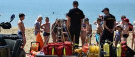 Na zdjęciu strażacy i policjanci oraz dzieci podczas pogadanki na plaży