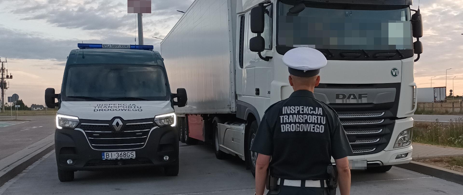 Na pierwszym planie: umundurowany inspektor podlaskiej Inspekcji Transportu Drogowego stoi przez oznakowanym furgonem ITD i zatrzymanym do kontroli ciągnikiem siodłowym z podpiętą naczepą-chłodnią.