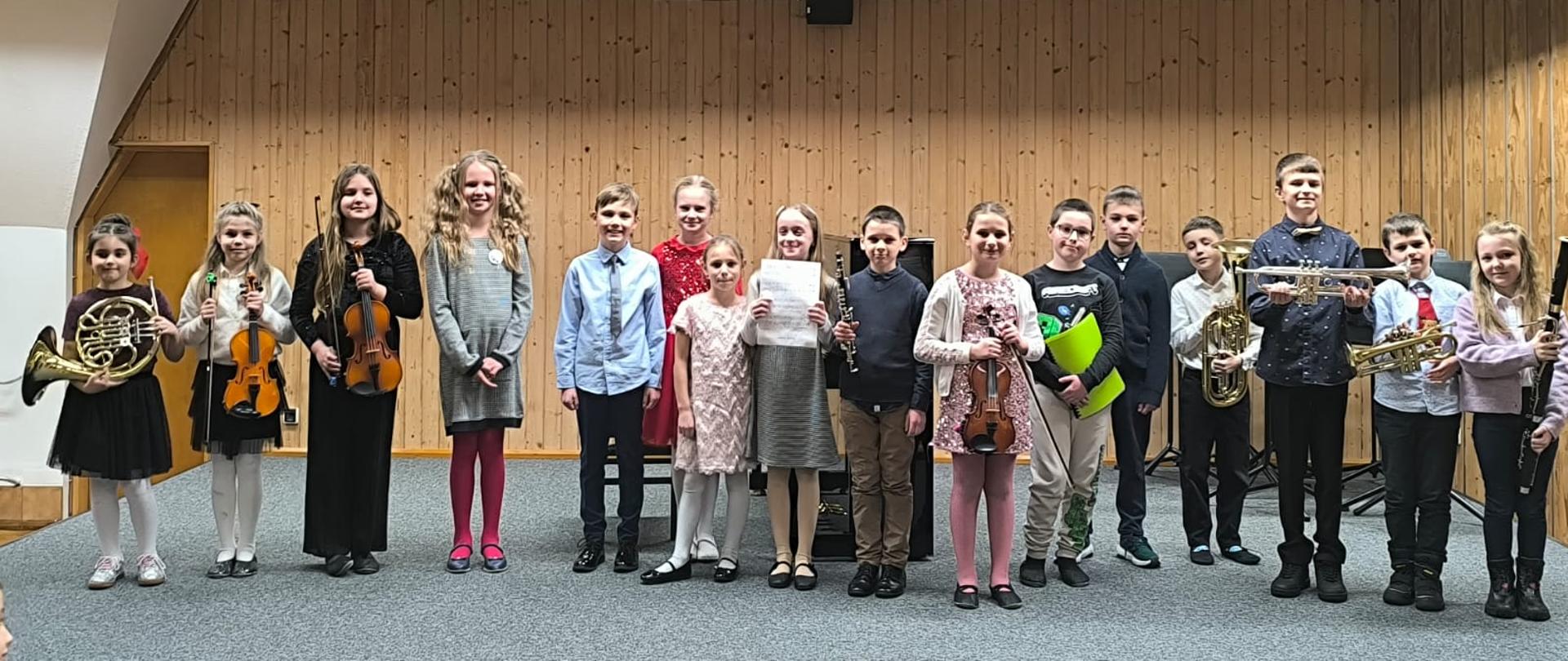 Wszyscy wykonawcy, grupa kilkunastu dzieci, stoi na scenie ze swoimi instrumentami.