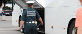 Inspektor mazowieckiej Inspekcji Transportu Drogowego kontroluje autokar przed wyjazdem w trasę z grupą dzieci i młodzieży.