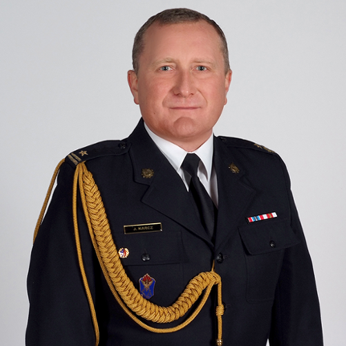 Na zdjęciu młodszy brygadier Jacek Karcz, Komendant Powiatowy Państwowej Straży Pożarnej w Pabianicach. Występuje w umundurowaniu wyjściowym ze sznurem. Na lewej piersi przypięte baretki. Na prawej piersi od góry znajduje się imiennik, absolwentka Szkoły Głównej Służby Pożarniczej oraz absolwentka Szkoły Aspirantów w Poznaniu.