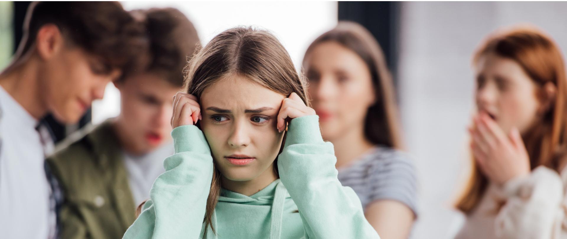Na zdjęciu na pierwszym planie jest dziewczyna trzymająca się za głowę. W tle widać dwójkę chłopaków patrzących ze dziwieniem w telefon oraz dwie zaskoczone dziewczyny.