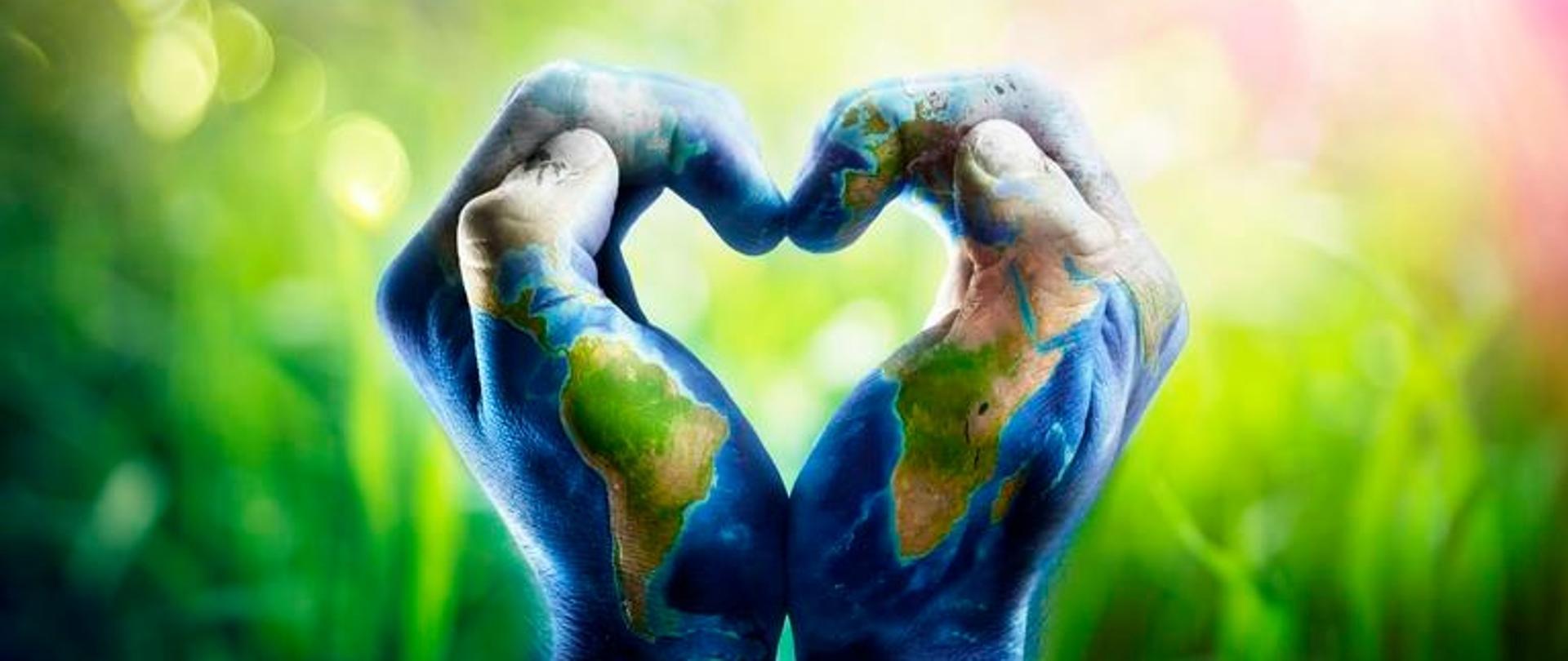 Ludzkie ręce kształtujące serce. Ręce są pomalowane, wzorzyste i przedstawiają mapę świata na tle z przewagą zieleni.