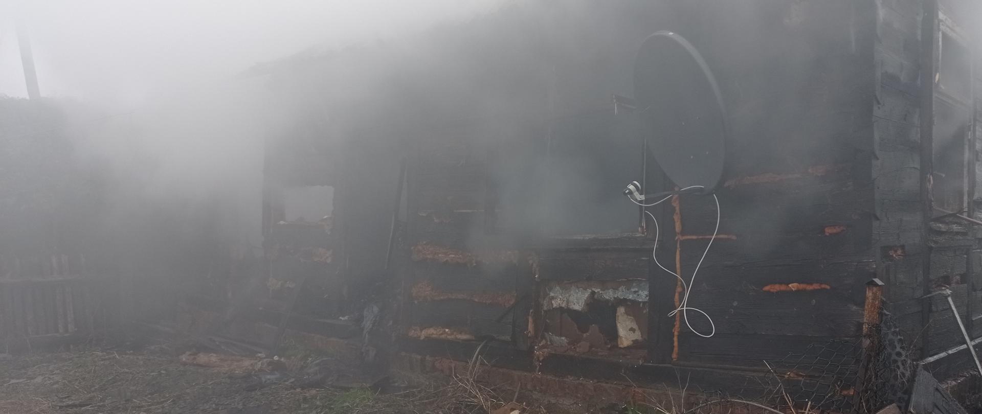 Front spalonego domu jednorodzinnego drewnianego. Z budynku wydobywa się dym